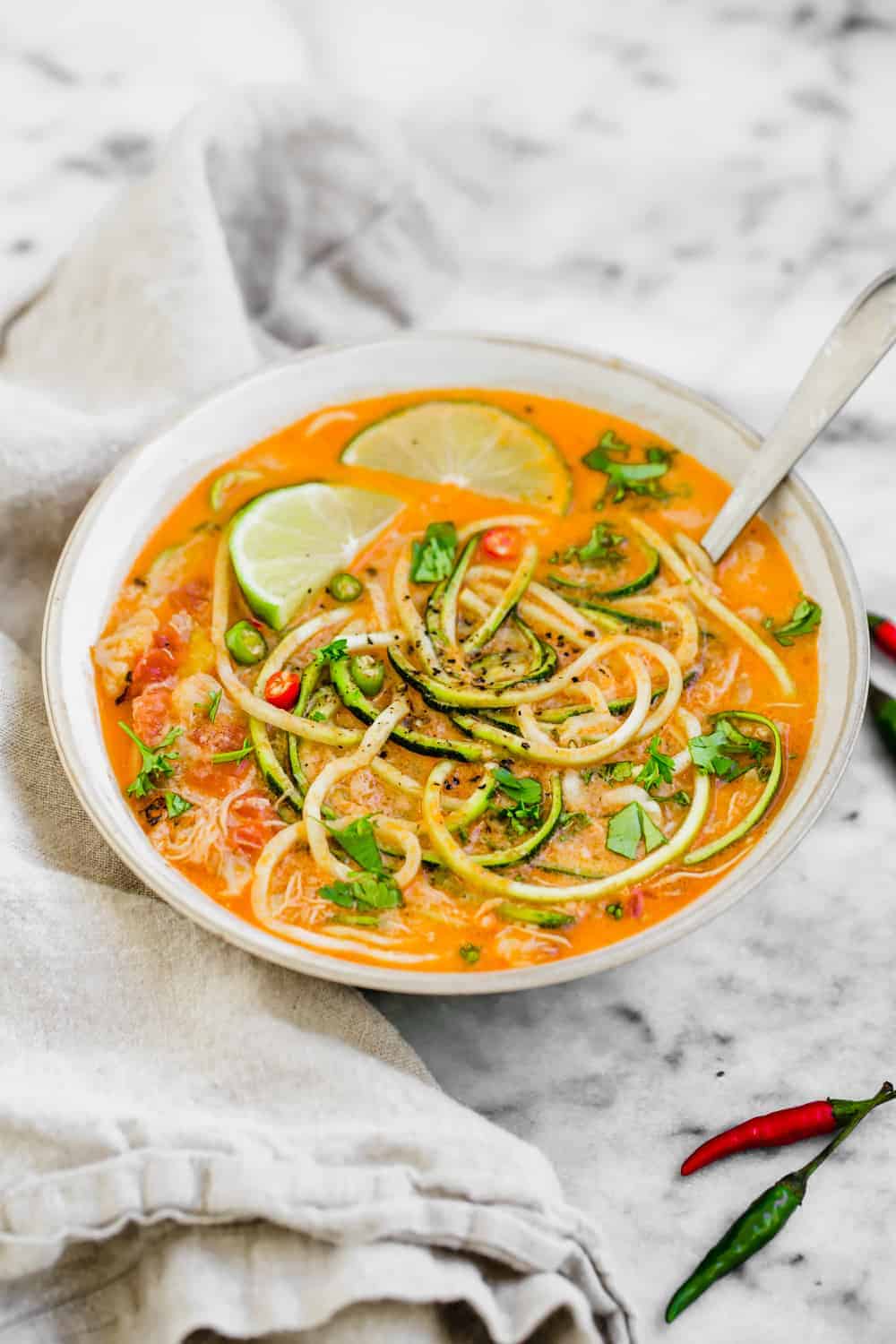 Thai chicken zucchini noodle soup in a white bowl with a spoon