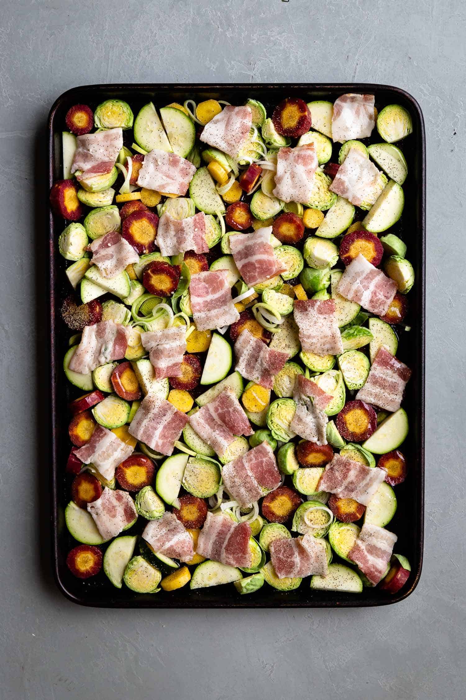 Raw chopped vegetables and sliced bacon in a sheet pan