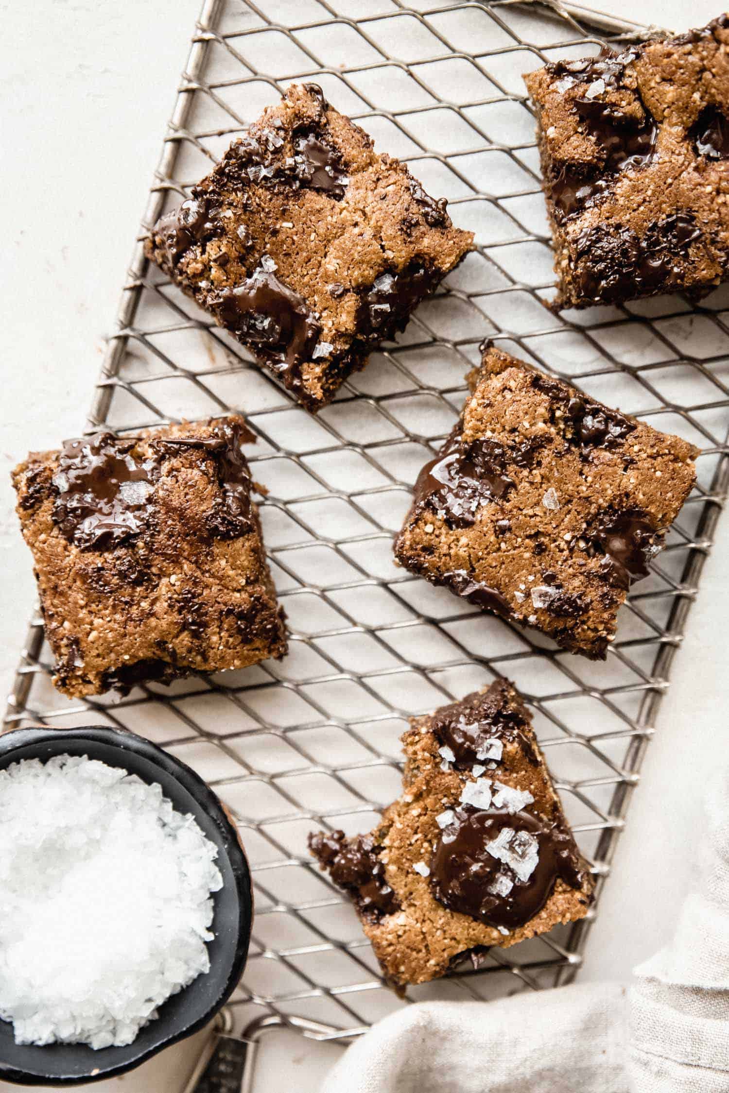 paleo chocolate chip blondies on a wire rack with a bowl of flaked salt