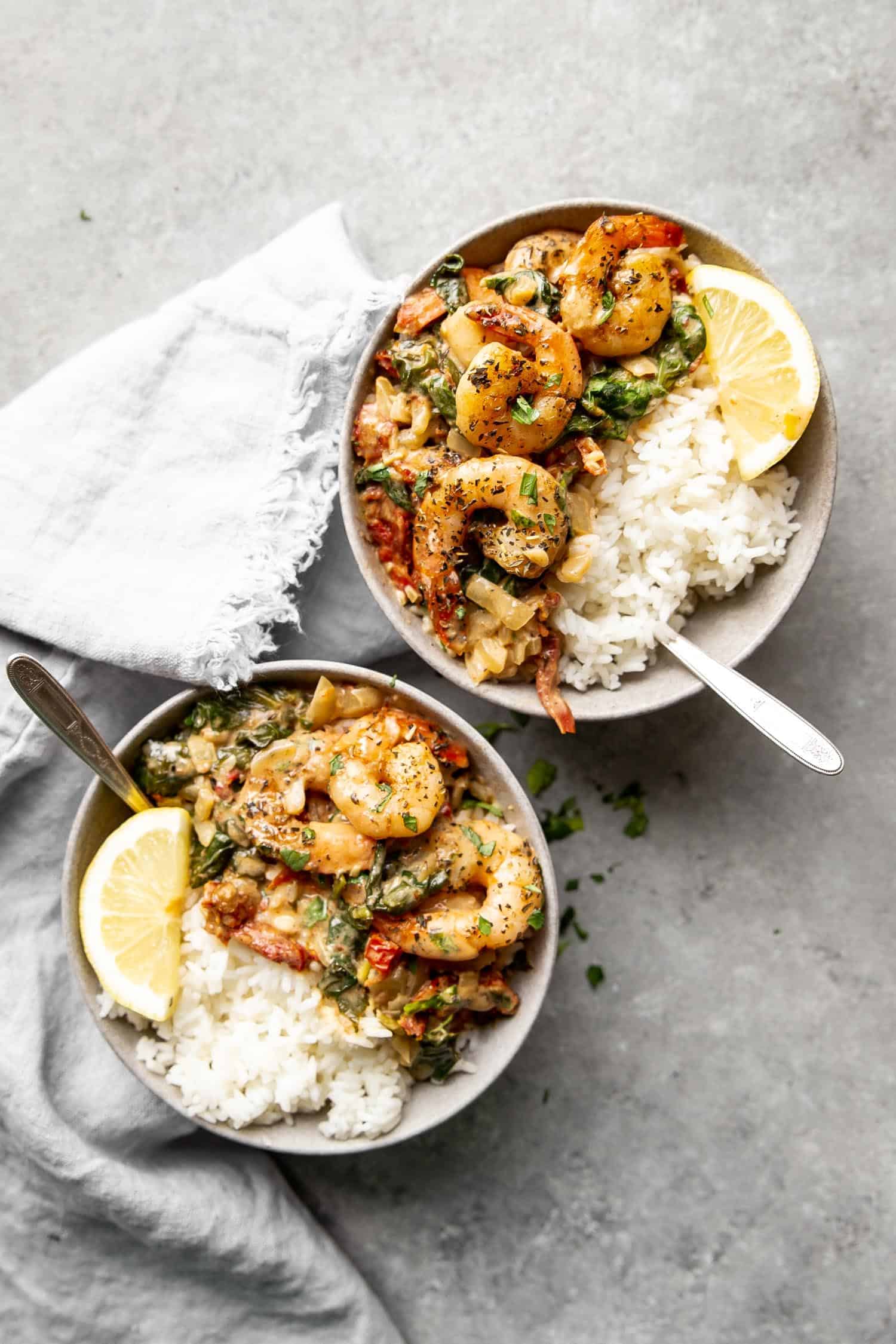 two bowls of creamy garlic shrimp with white rice and lemon wedges