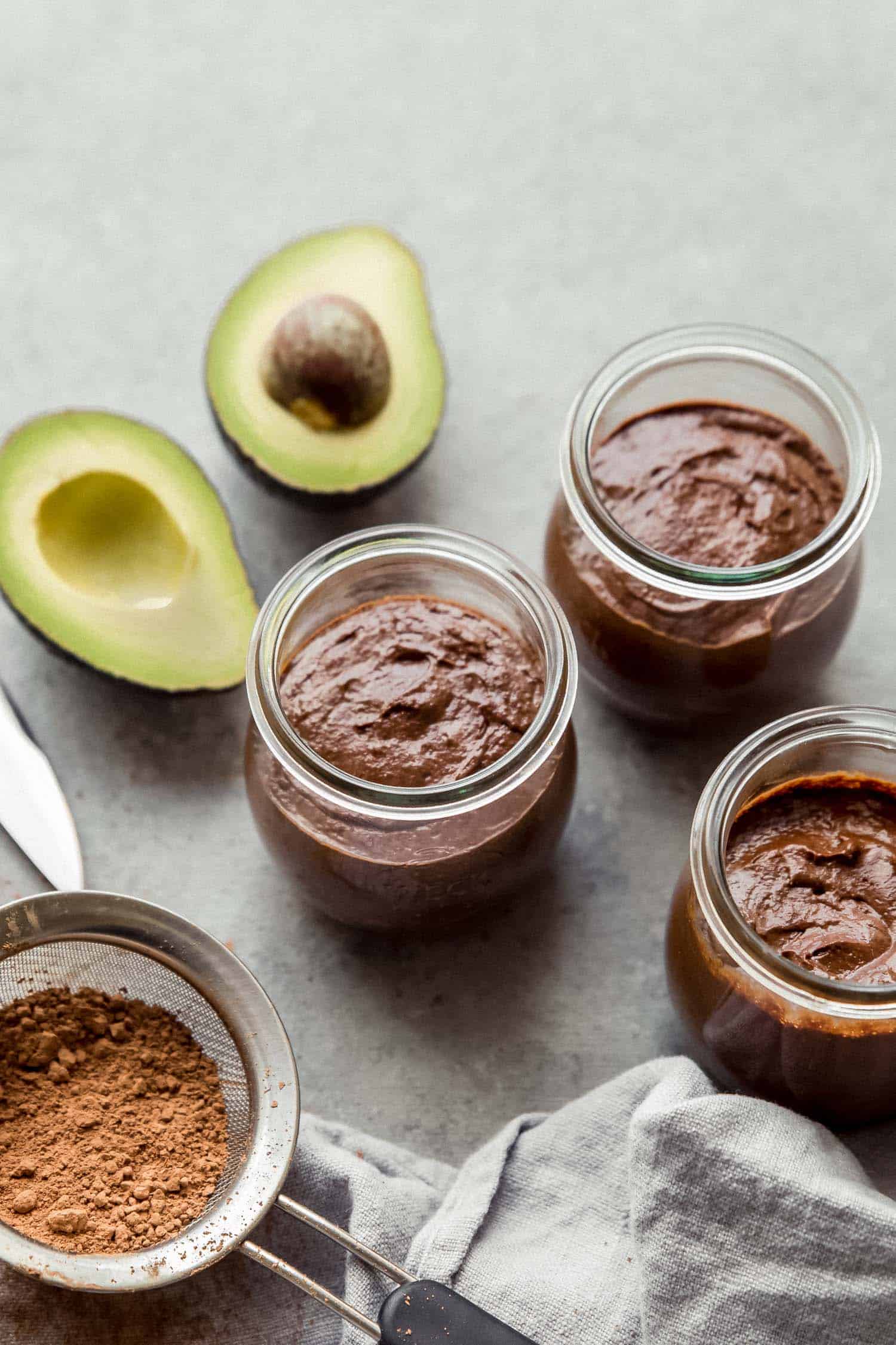 three jars of chocolate pudding with avocados and cacao powder
