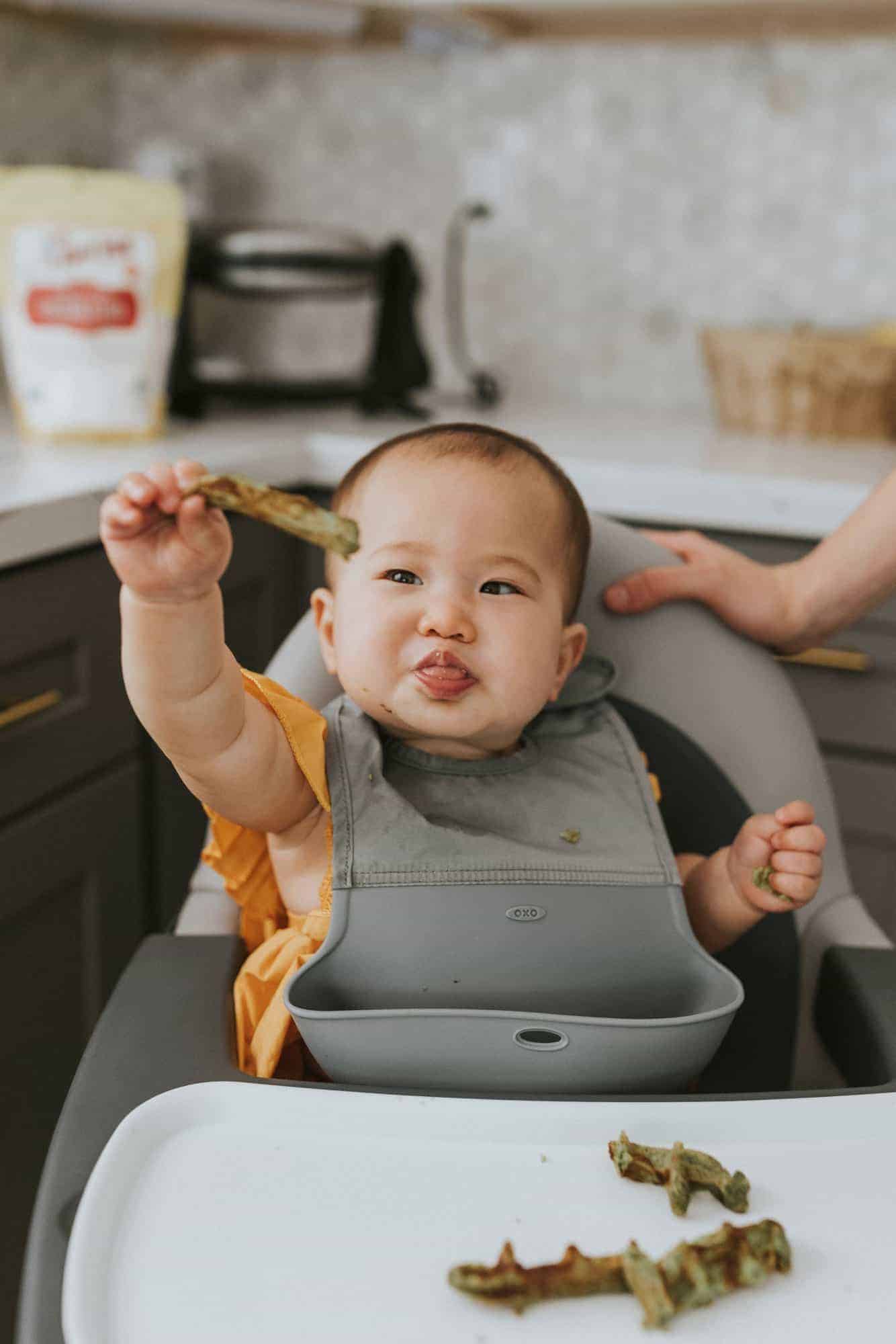 baby eating spinach bone broth waffles in a high chair