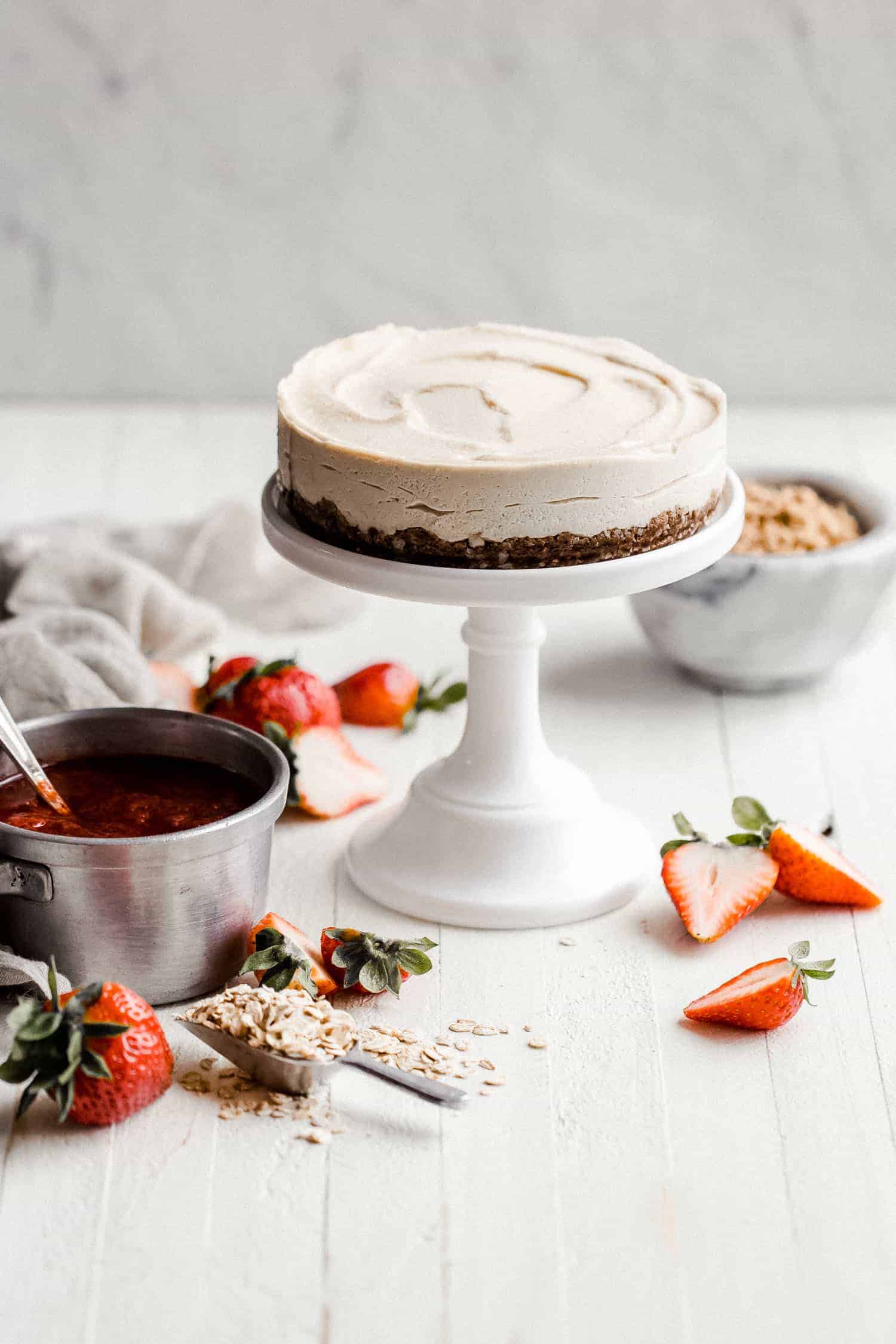 vegan cheesecake on a cake stand with strawberry sauce on the side