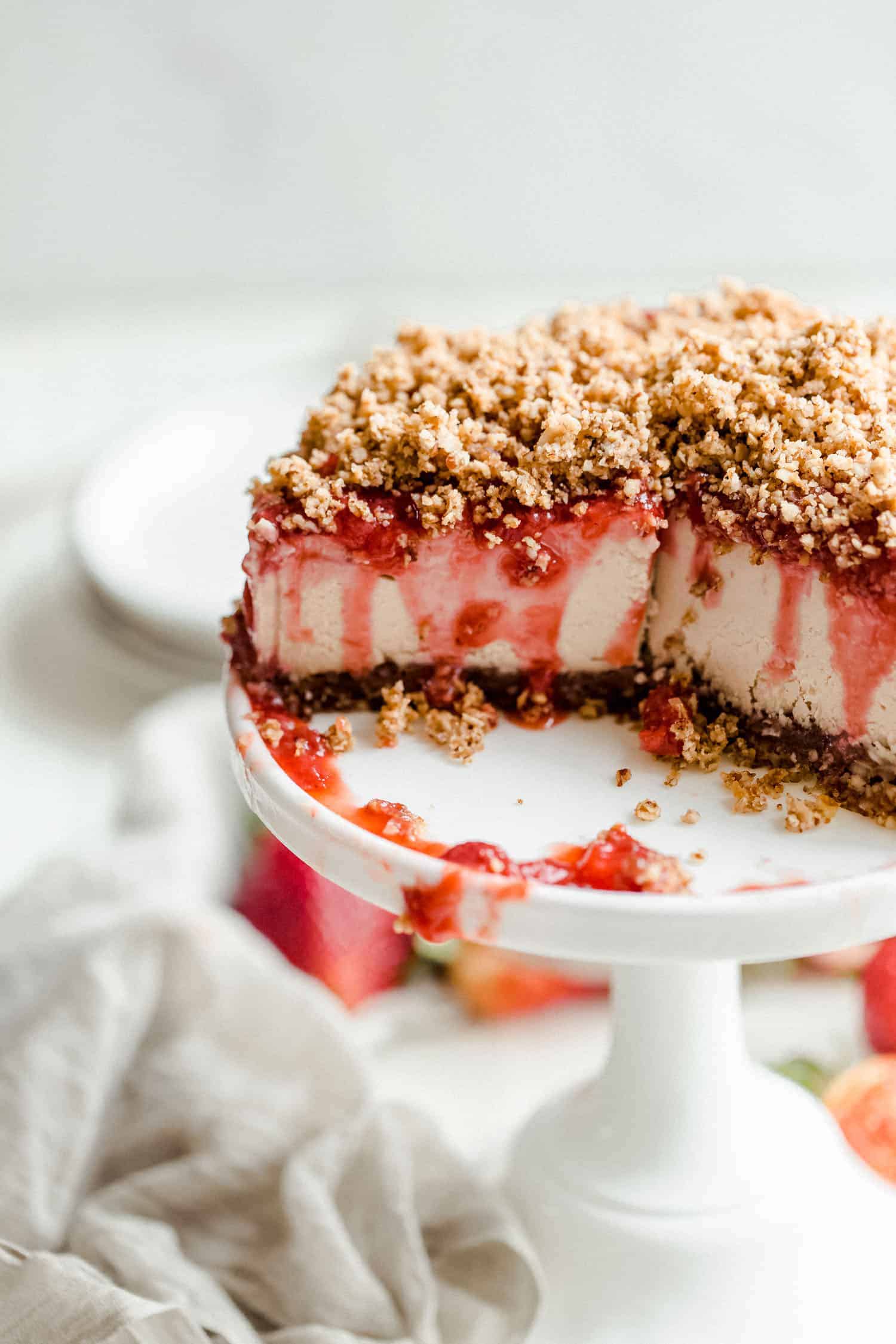 vegan strawberry cheesecake with slice removed on a white cake stand
