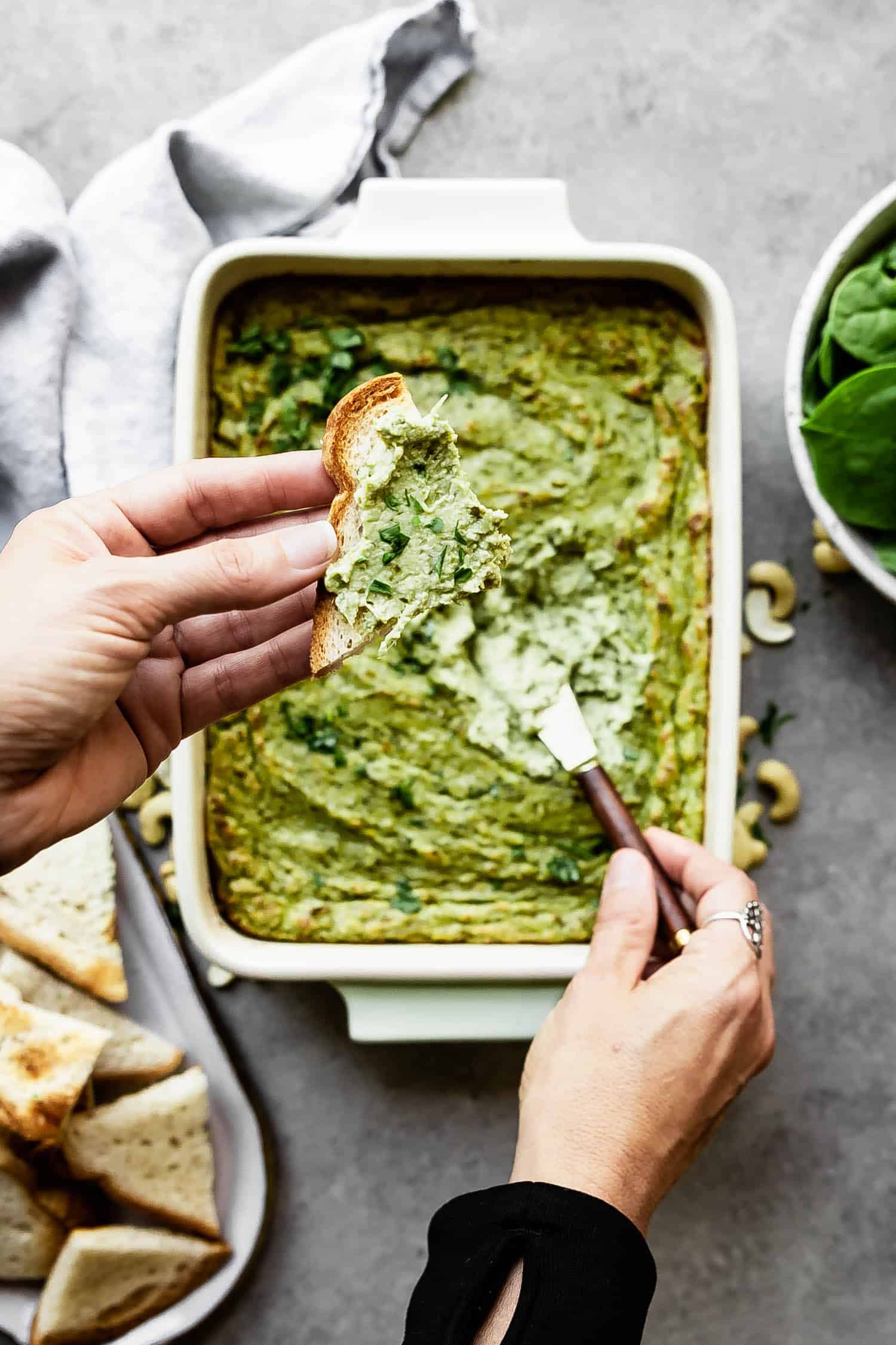 spinach artichoke dip being dipped into with a small knife