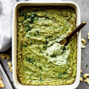 vegan spinach artichoke dip in a baking dish with a small knife inside