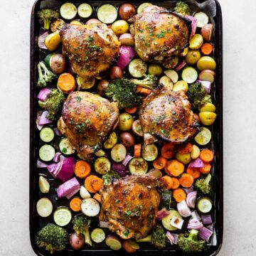 chicken thighs on a bed of veggies on top of a baking sheet