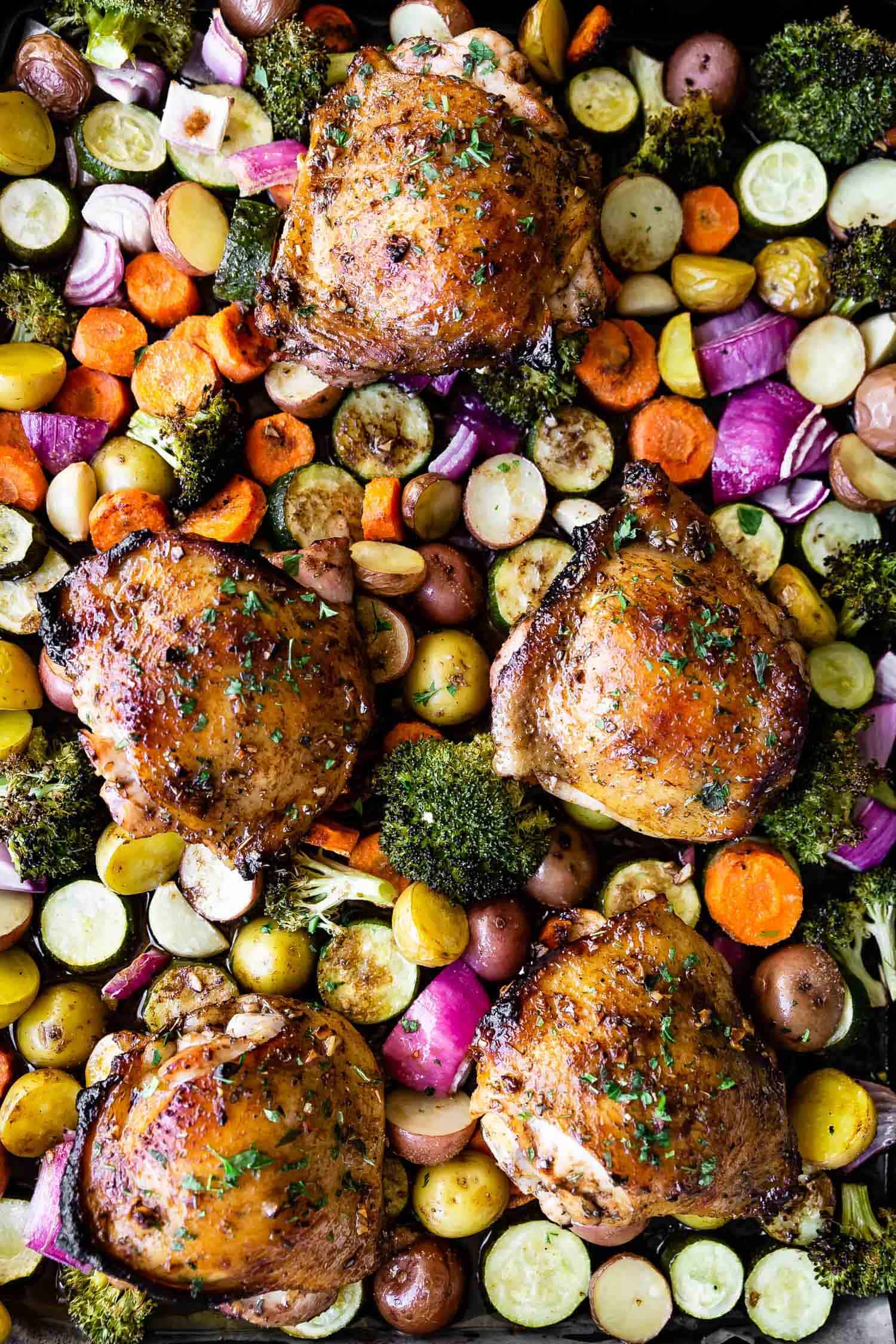 close up of roasted chicken thighs and vegetables on a sheet pan