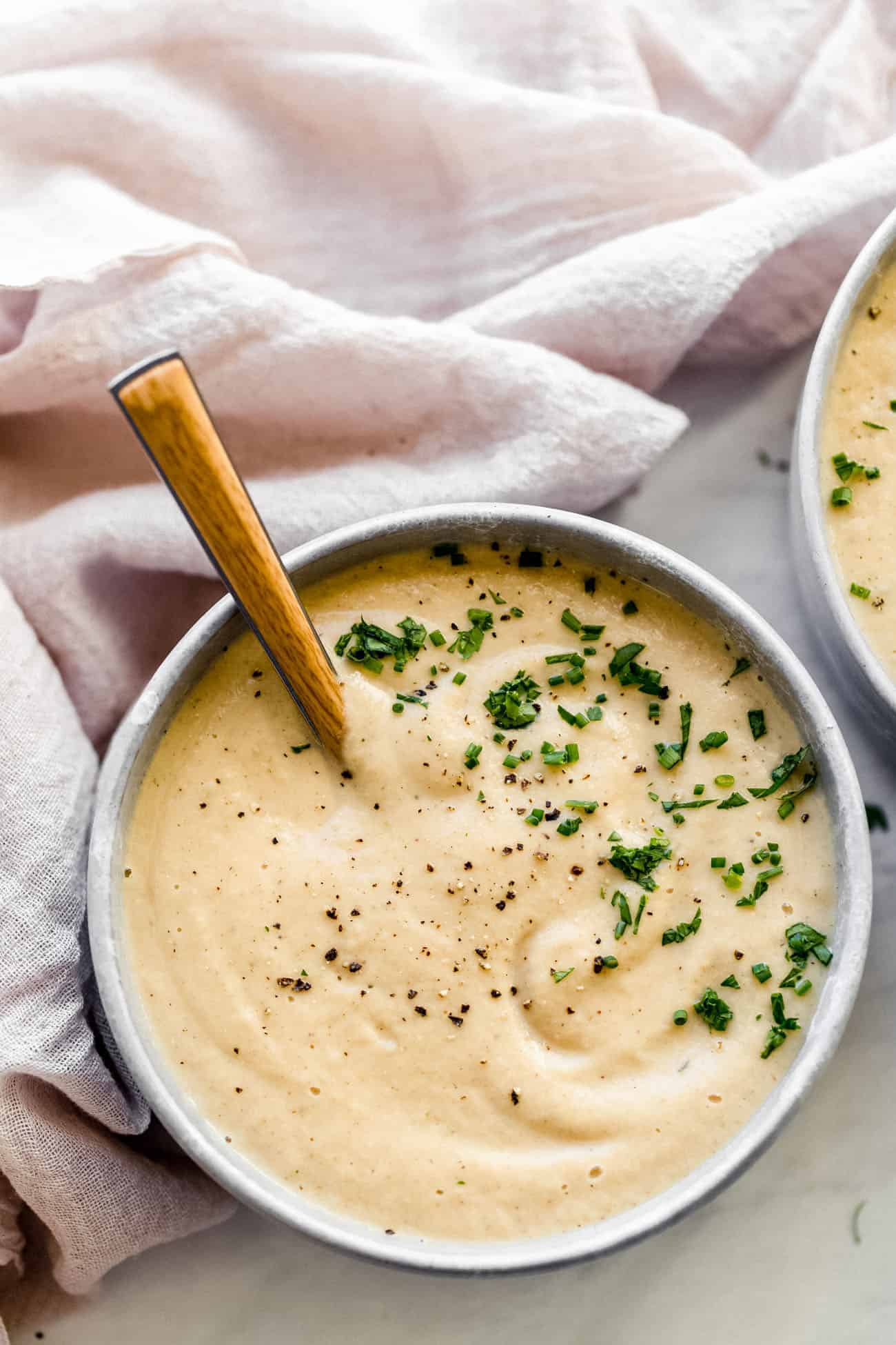 a bowl of cauliflower soup with parsley on top and a spoon inside