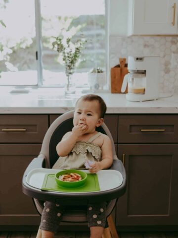 baby eating food in a white and gray high chair in the kitchen