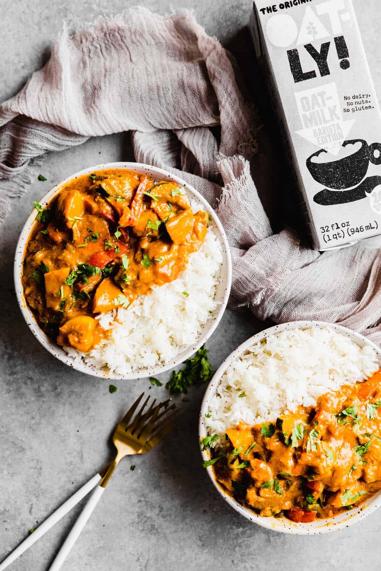 two bowls of Thai red curry with white rice and a container of Oatly