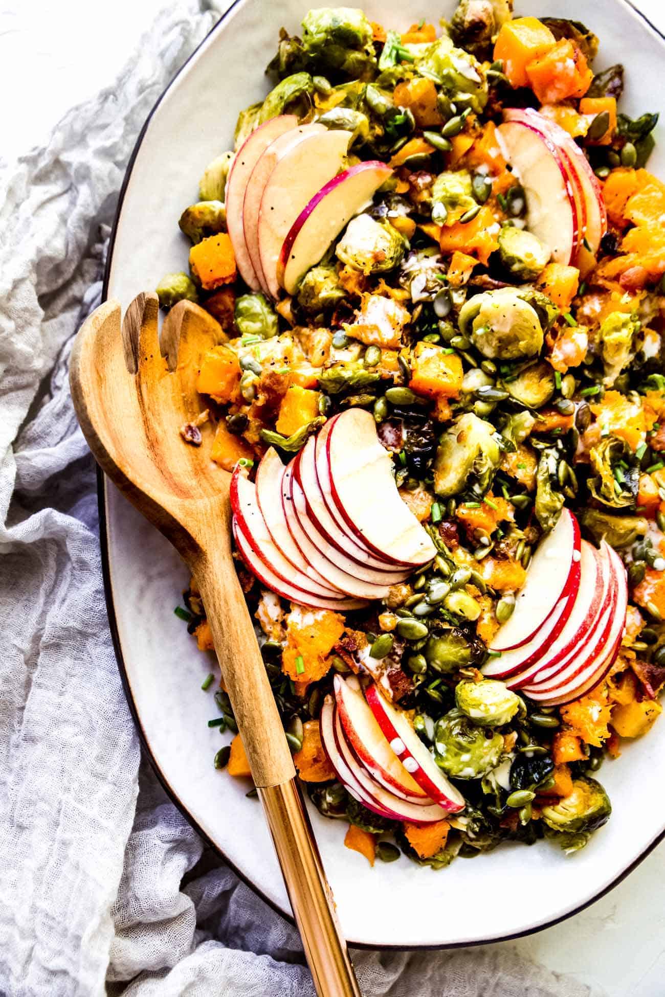 roasted brussels sprouts and butternut squash on a white platter with a wooden spoon