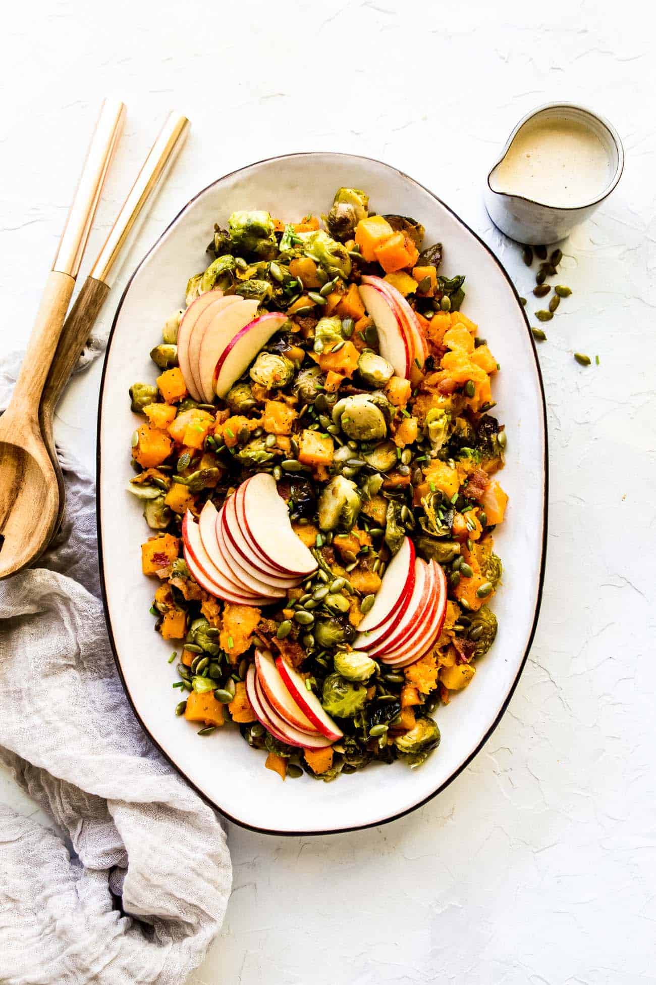 roasted butternut squash and brussels sprouts on a platter with dressing on the side