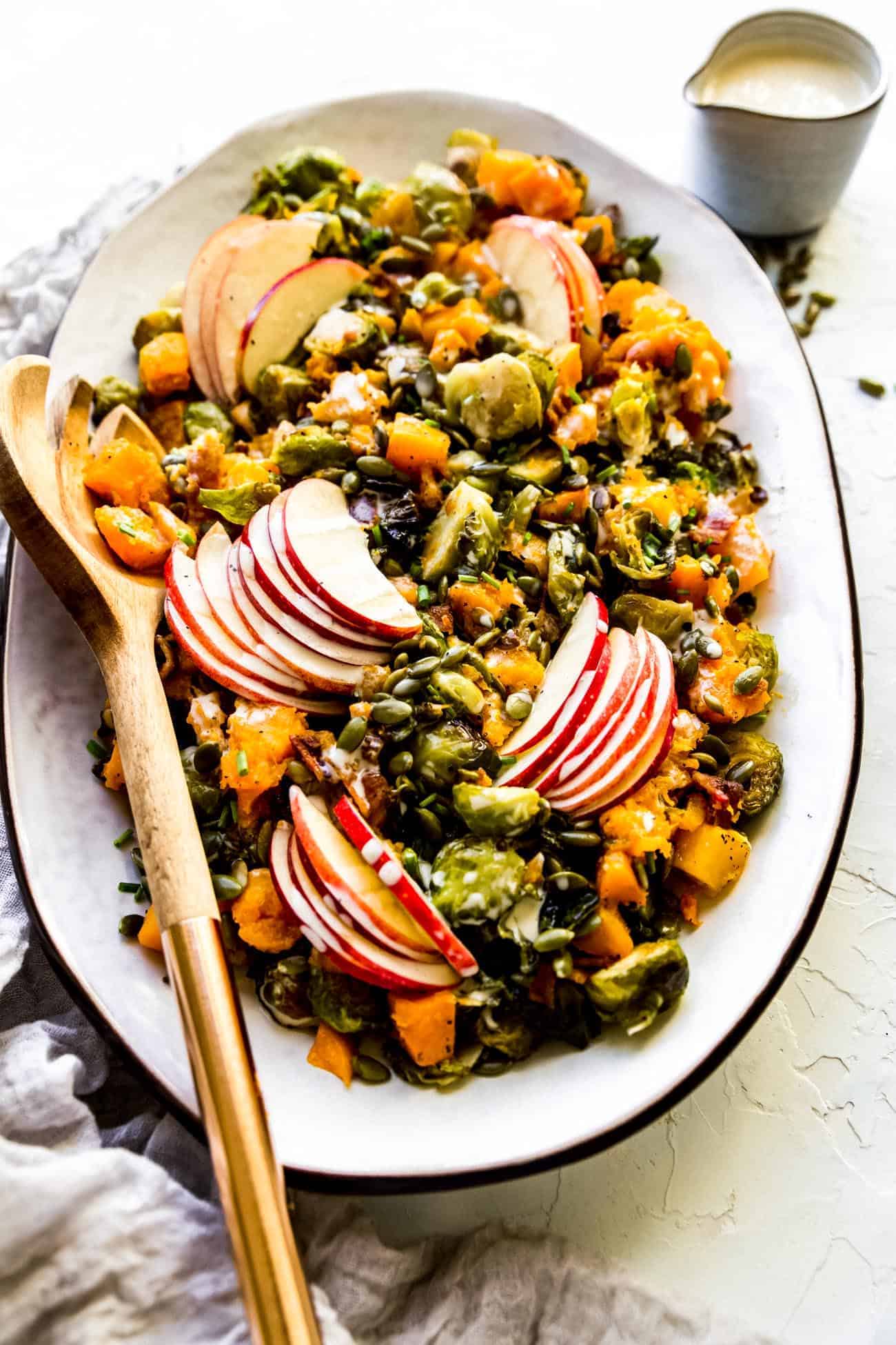roasted brussels sprouts and butternut squash on a white platter with a serving spoon