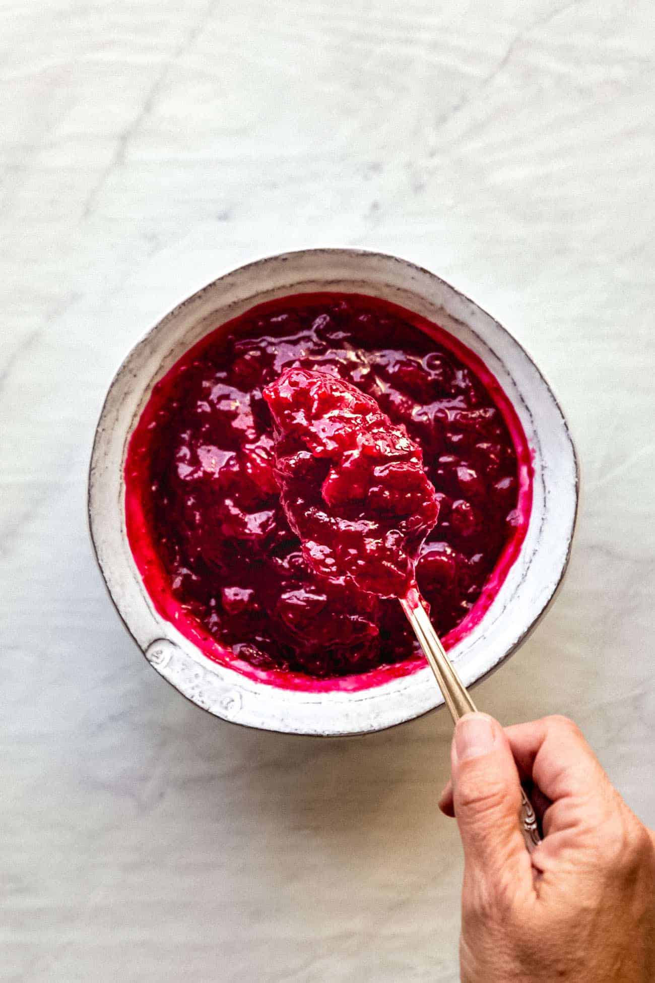 cranberry sauce in a white bowl with a spoon inside and some being scooped