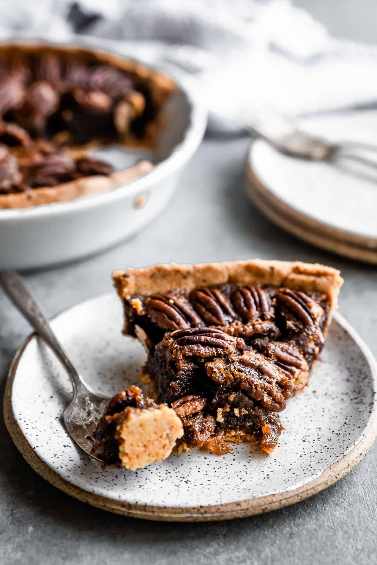 pecan pie on a white plate with a fork on the side and a bite taken out