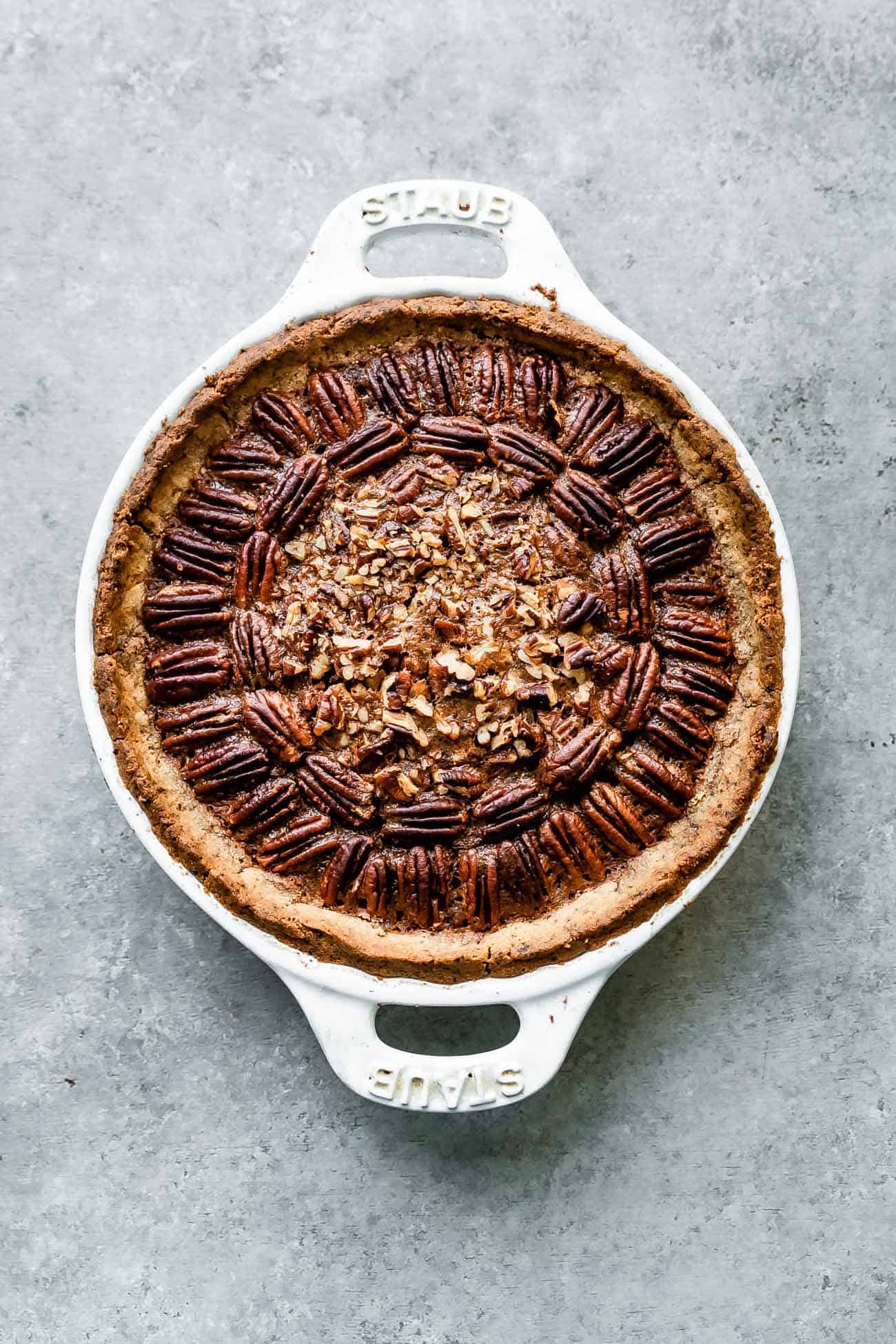 paleo pecan pie in a white pie plate with pecans on top