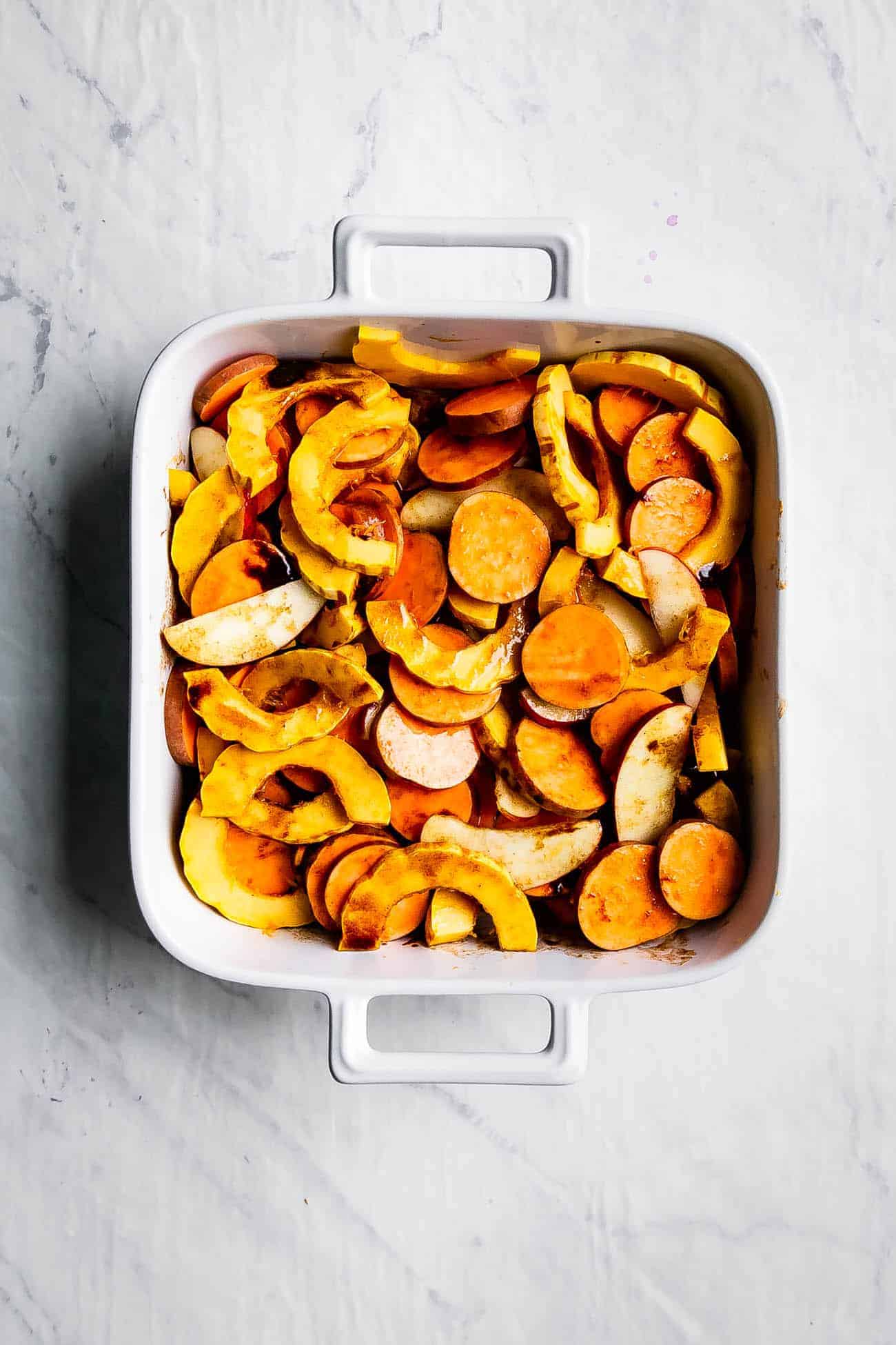 cut sweet potatoes, delicata squash, and apples in a white casserole dish