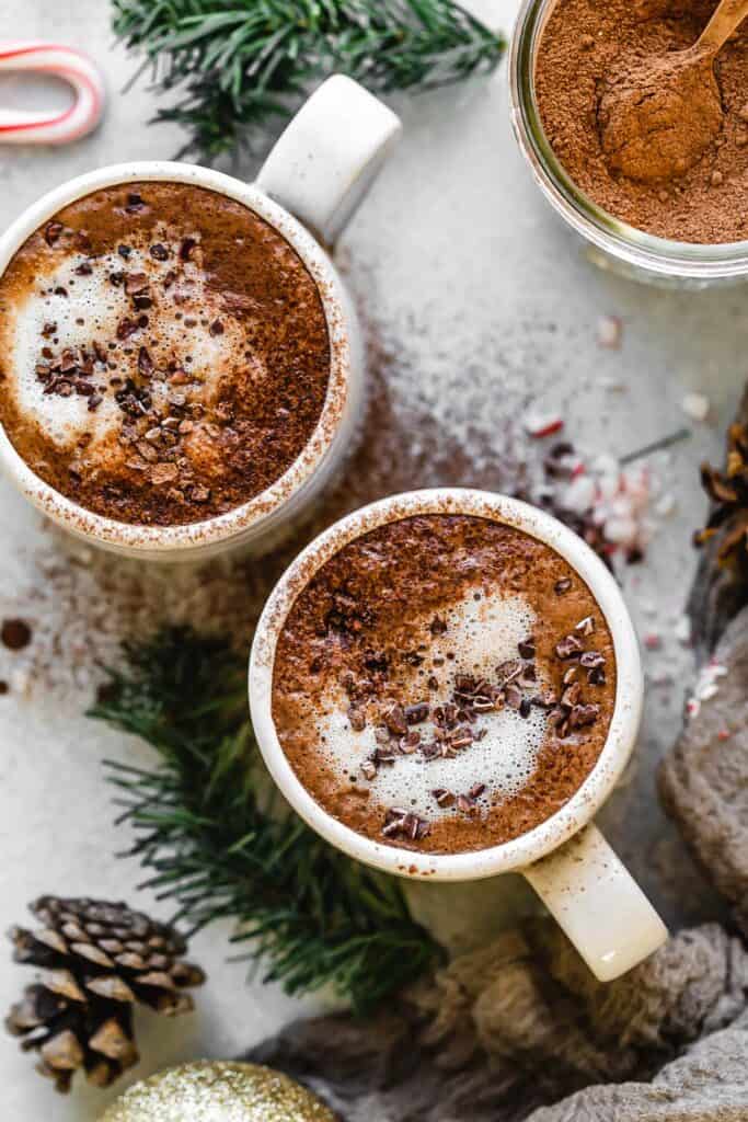 two mugs of dairy free peppermint hot chocolate with cacao nibs and foam