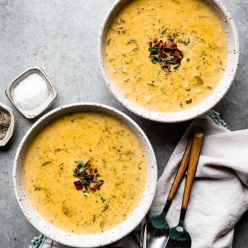two bowls of broccoli cheddar soup with bacon and parsley on top