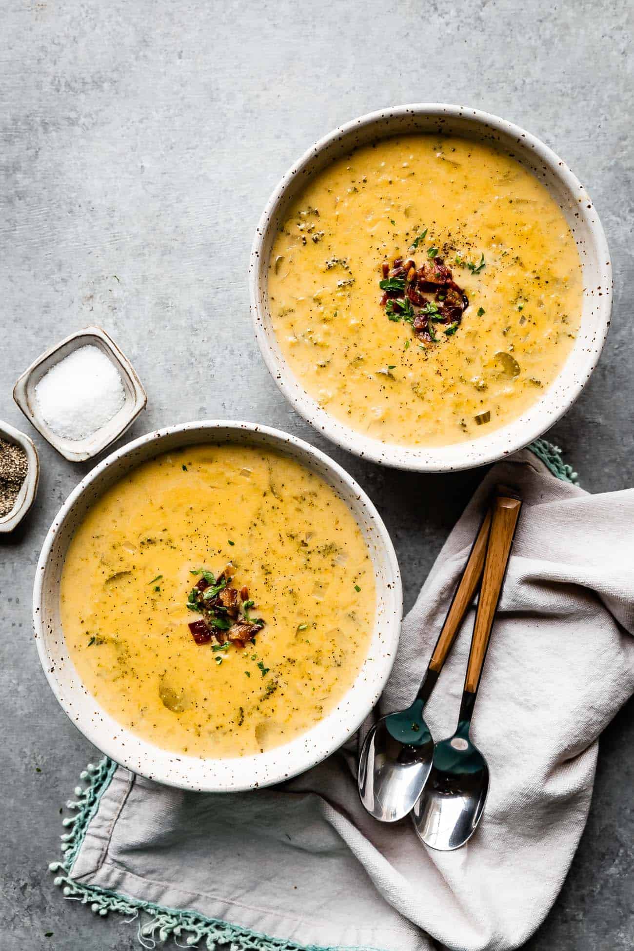 two bowls of broccoli cheddar soup with bacon and parsley on top