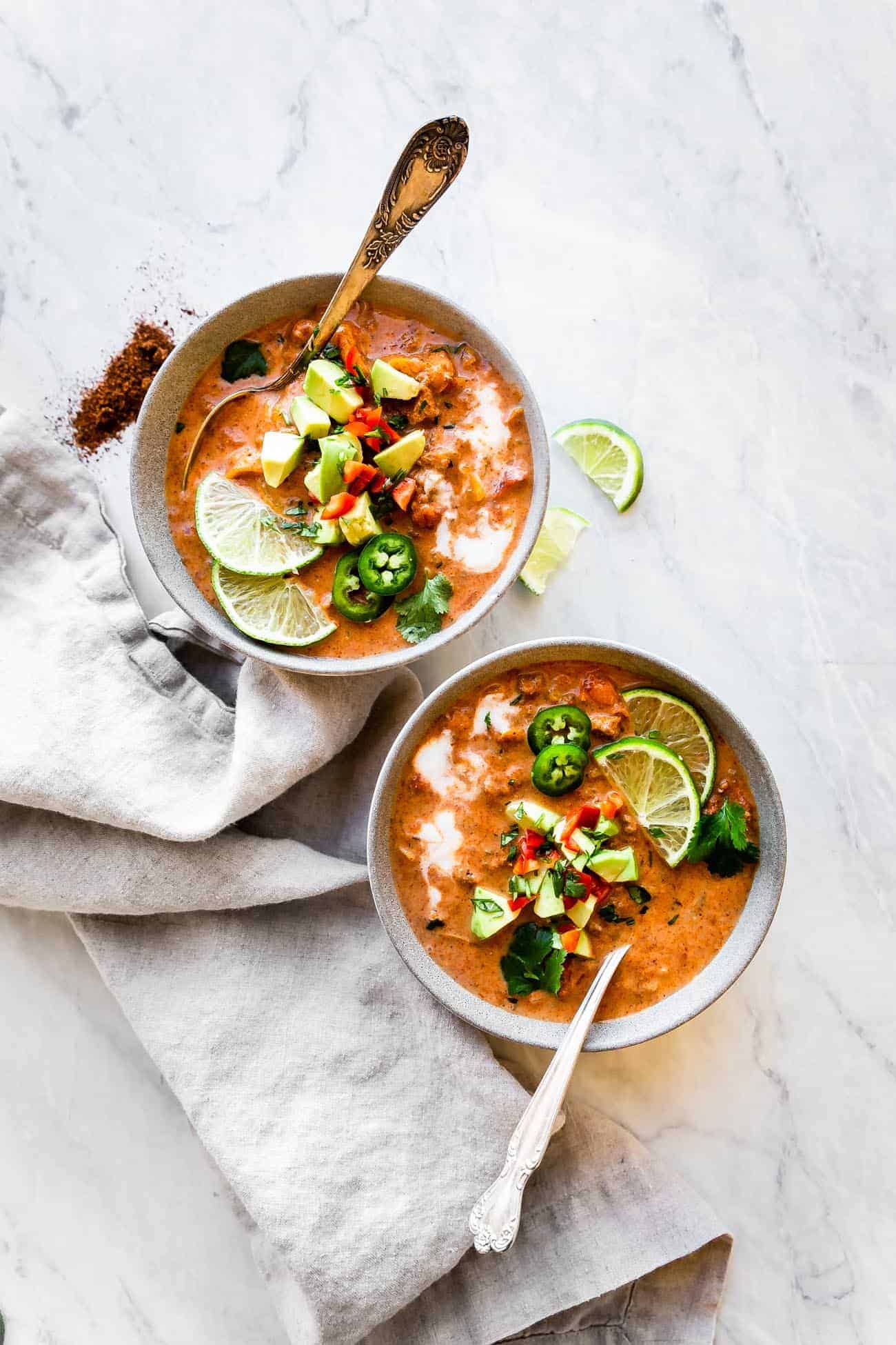 two bowls of taco soup with spoons inside and topped with avocado and limes