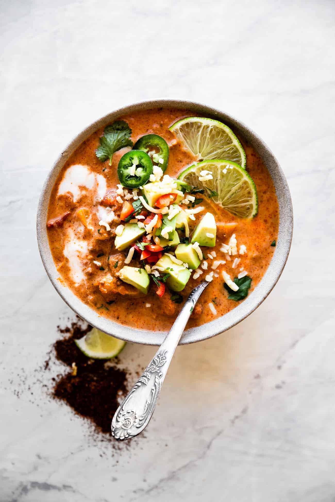 bowl of creamy taco soup with a spoon inside and avocado and limes on top