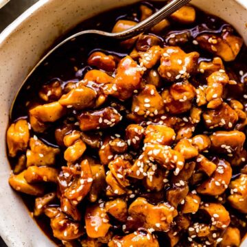 sesame chicken in a bowl with a spoon inside and sesame seeds on top