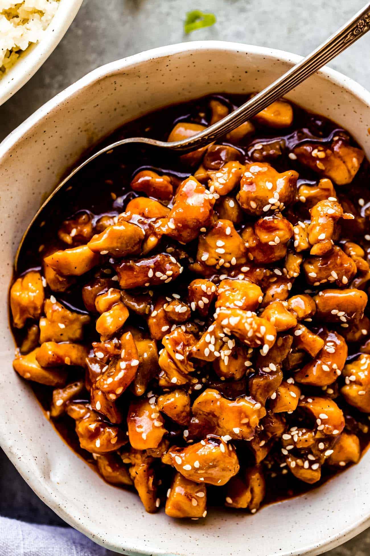 sesame chicken in a bowl with a spoon inside and sesame seeds on top