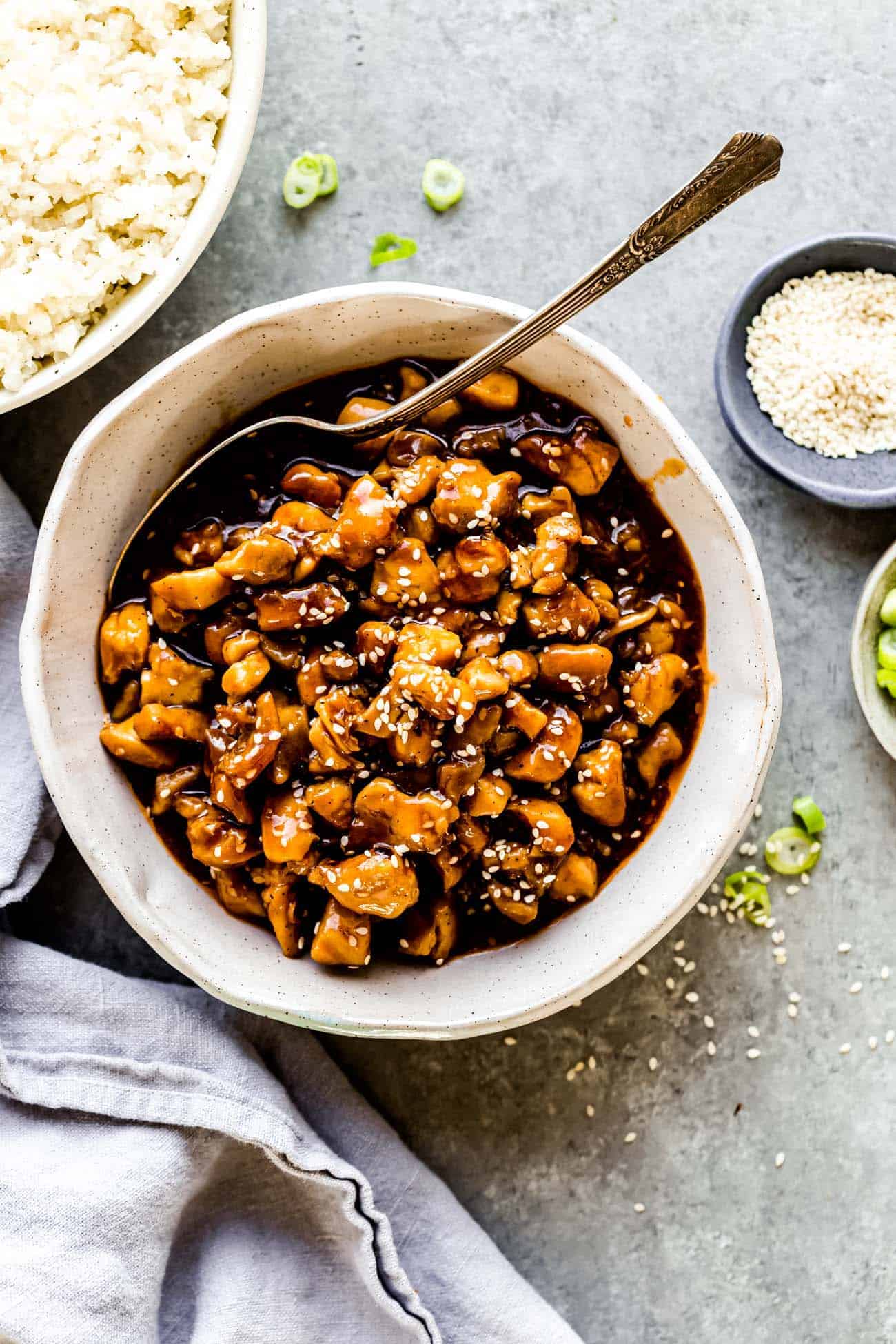 sesame chicken with a spoon inside a bowl and rice on the side