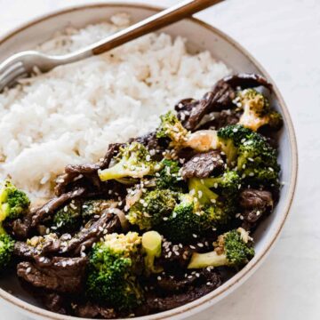 beef and broccoli on a plate with white rice and a fork inside