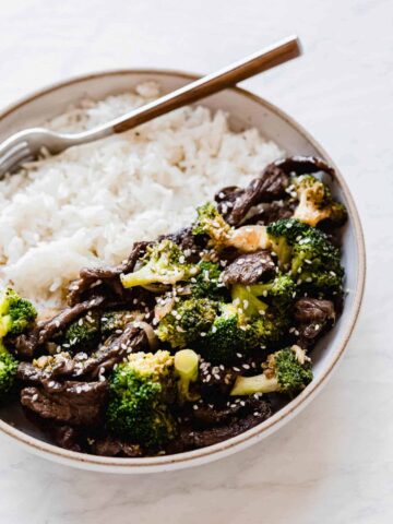 beef and broccoli on a plate with white rice and a fork inside