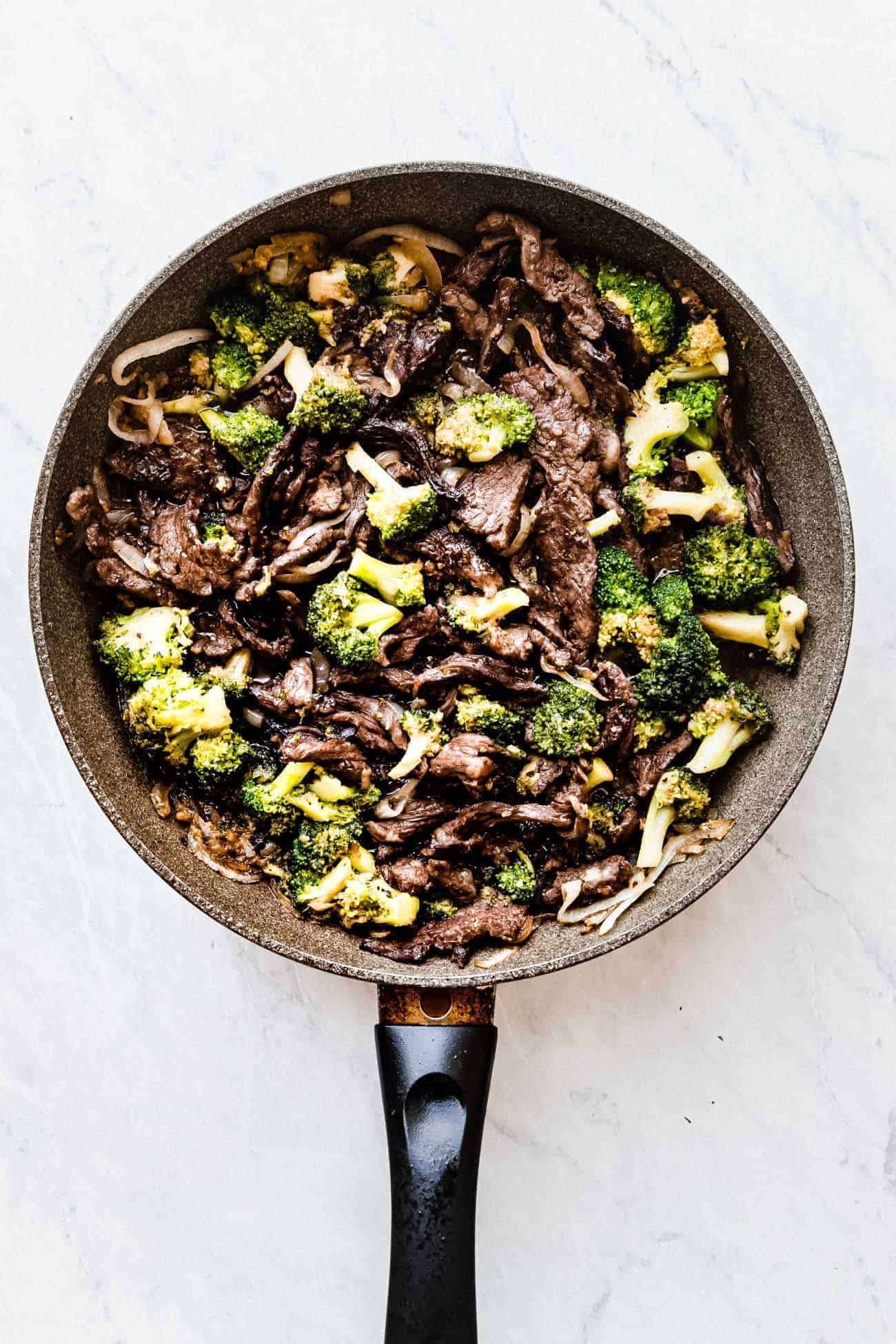 beef and broccoli in a frying pan with sesame seeds on top