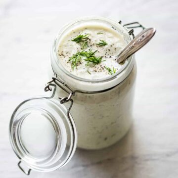 vegan tzatziki sauce in a glass jar with a spoon inside and fresh dill