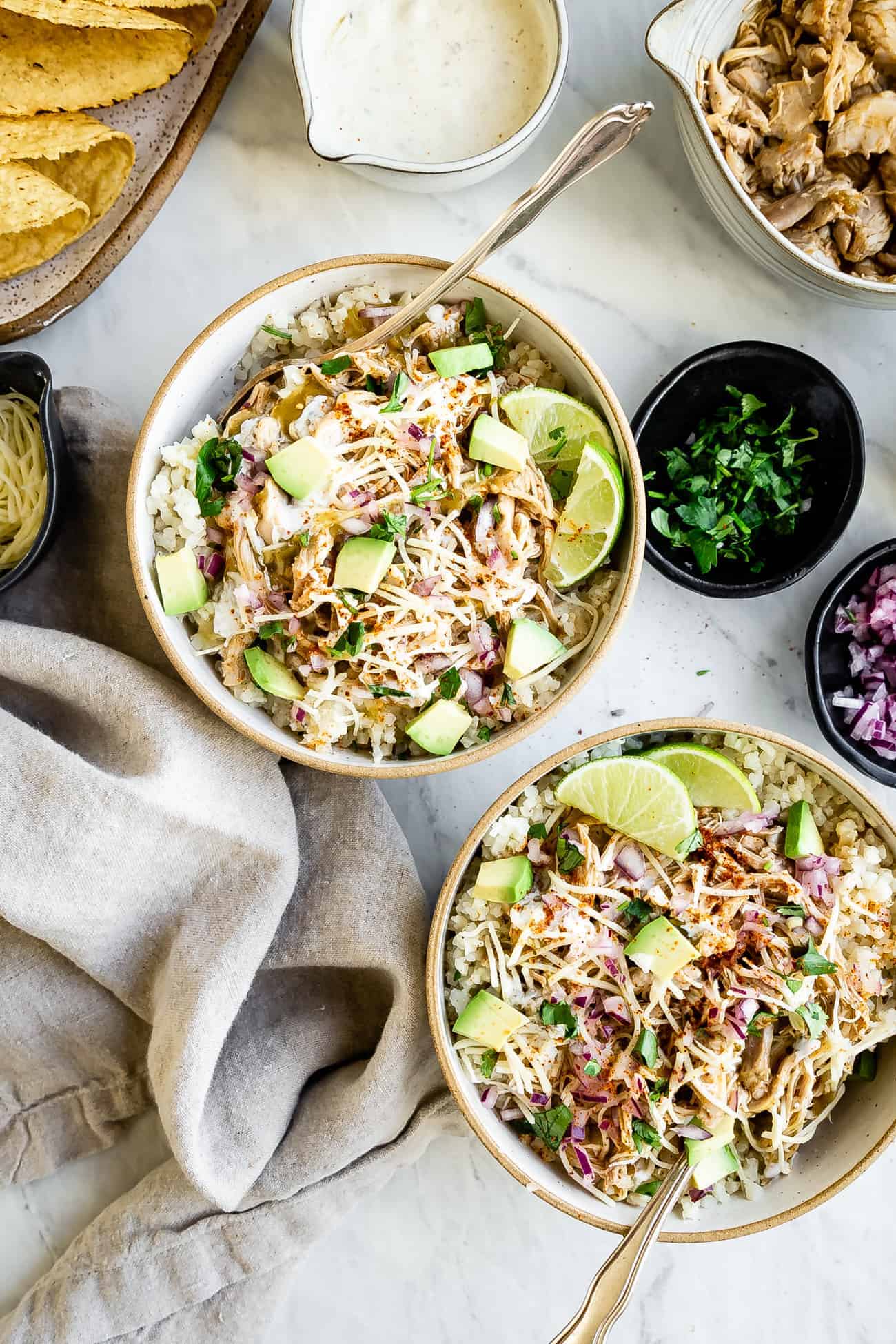 two chicken taco bowls with forks inside and ingredients around them