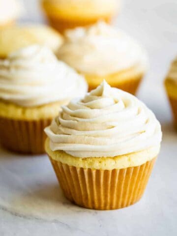 several vanilla cupcakes with vanilla buttercream frosting on top