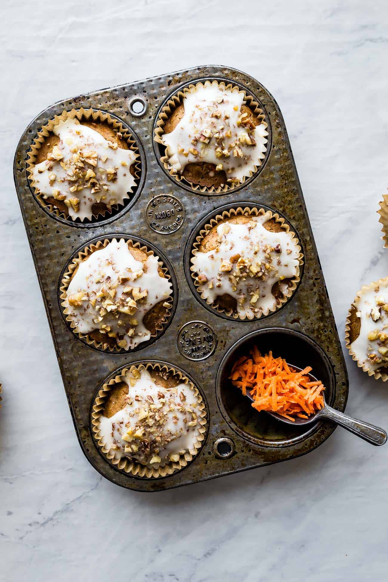 carrot cake muffins in a muffin tin with glaze and nuts on top