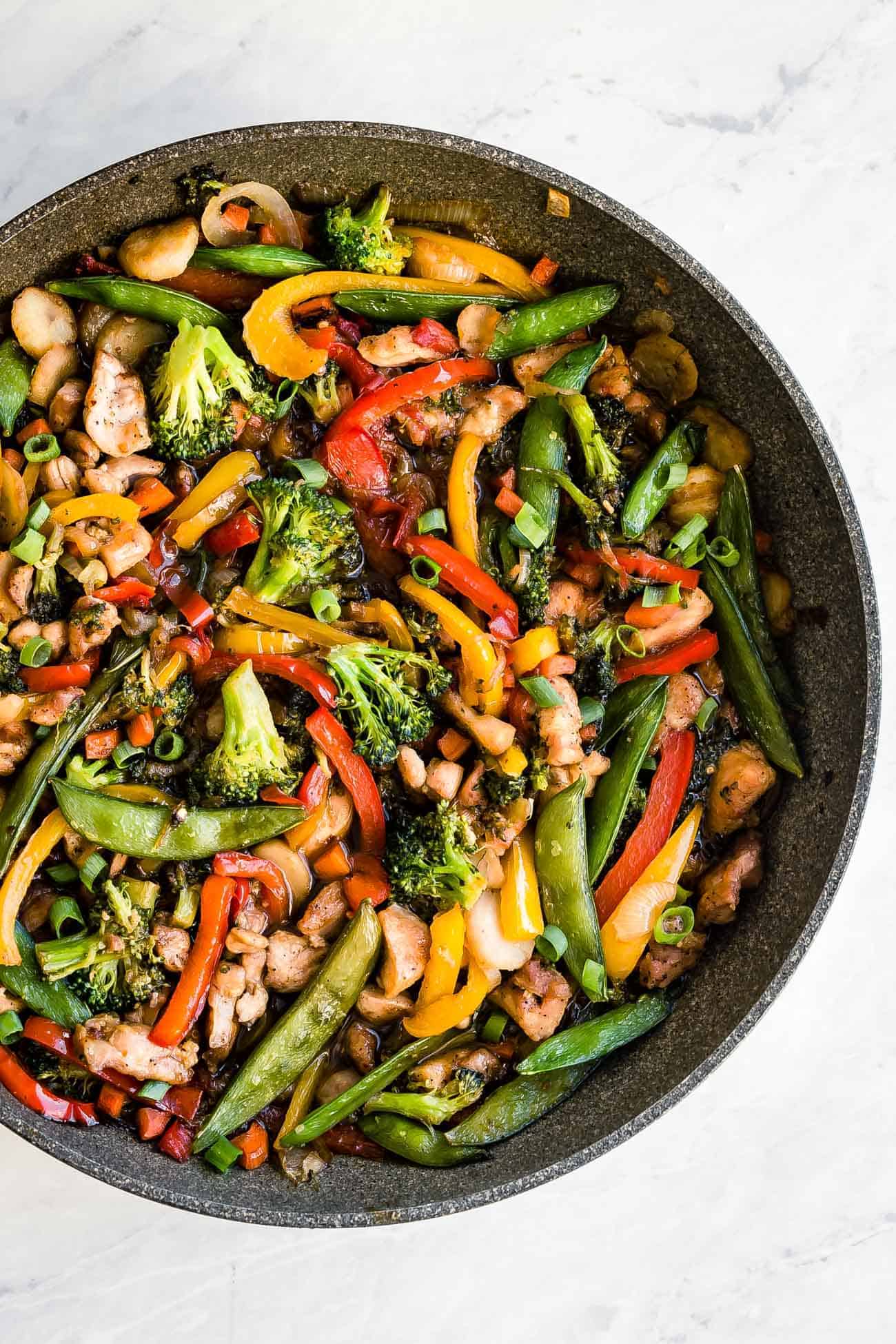 keto chicken stir fry in a saute pan with peppers, broccoli, carrots and snap peas