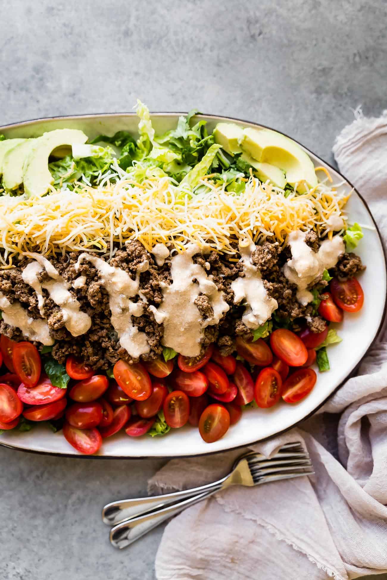 taco salad on a platter with dressing, cherry tomatoes, cheese, and avocado