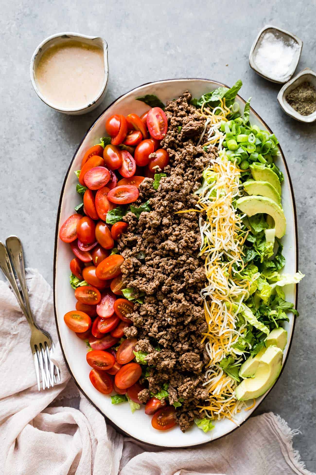 keto taco salad laid out on a platter with dressing on the side and salt and pepper
