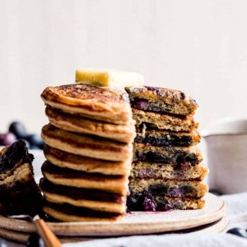 big stack of blueberry pancakes with a fork on the side and butter on top