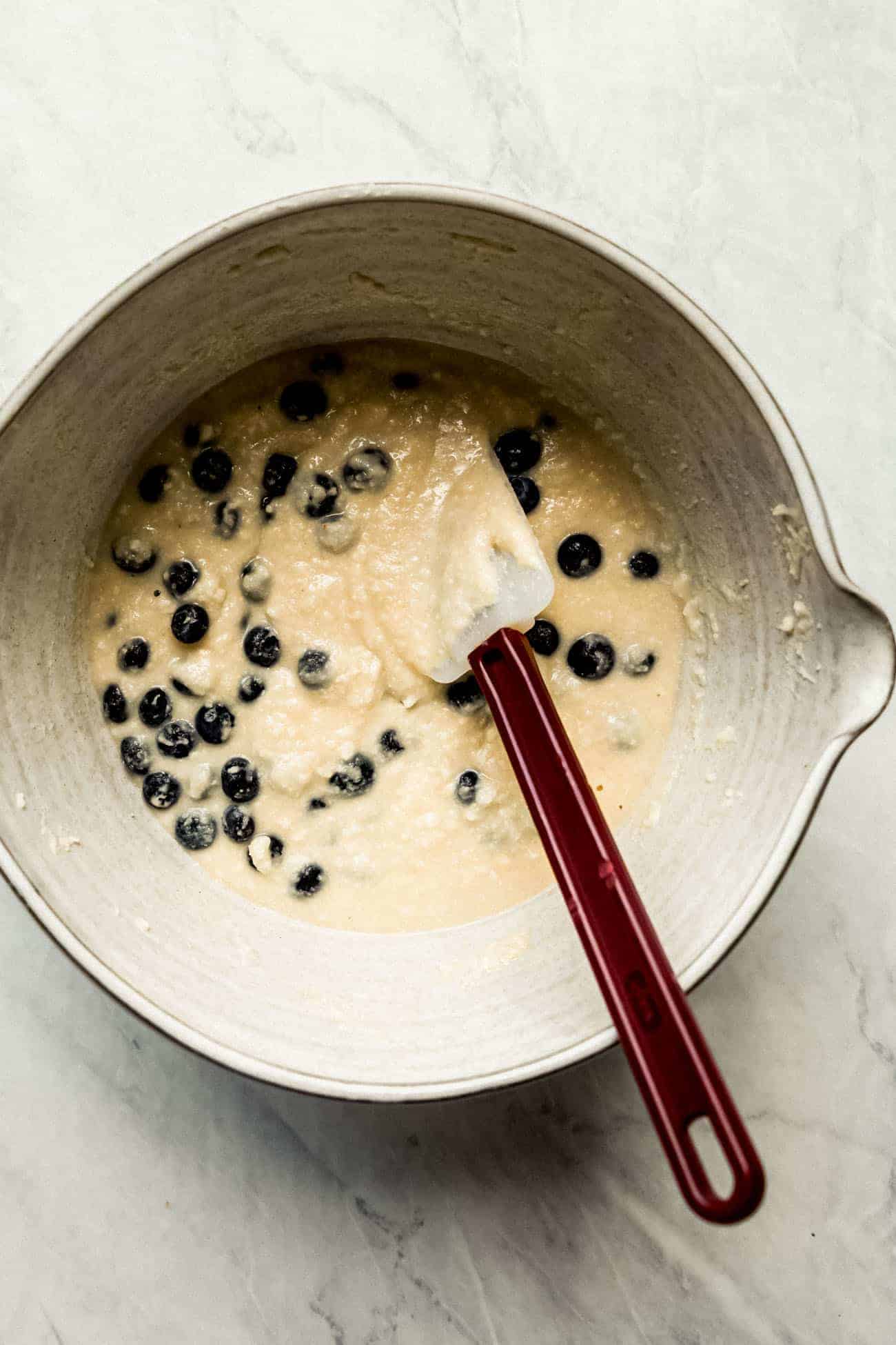 blueberry muffin batter in a white ceramic bowl with a spatula