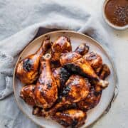 juicy barbecue chicken drumsticks on a plate with sauce on the side