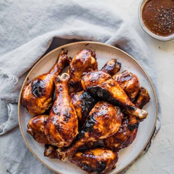 juicy barbecue chicken drumsticks on a plate with sauce on the side