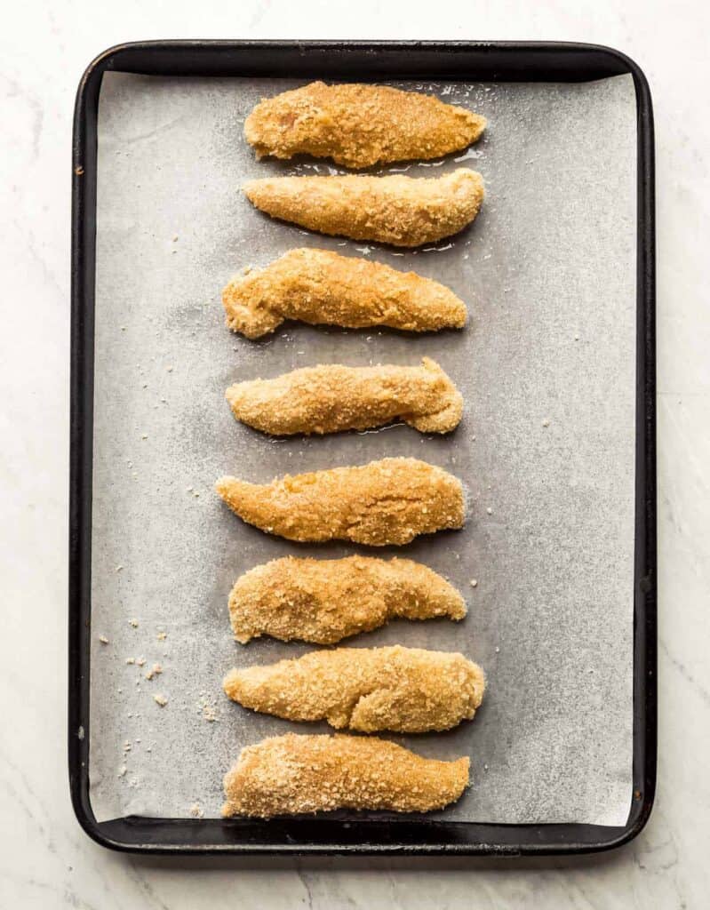 chicken strips laying on a parchment lined baking sheet