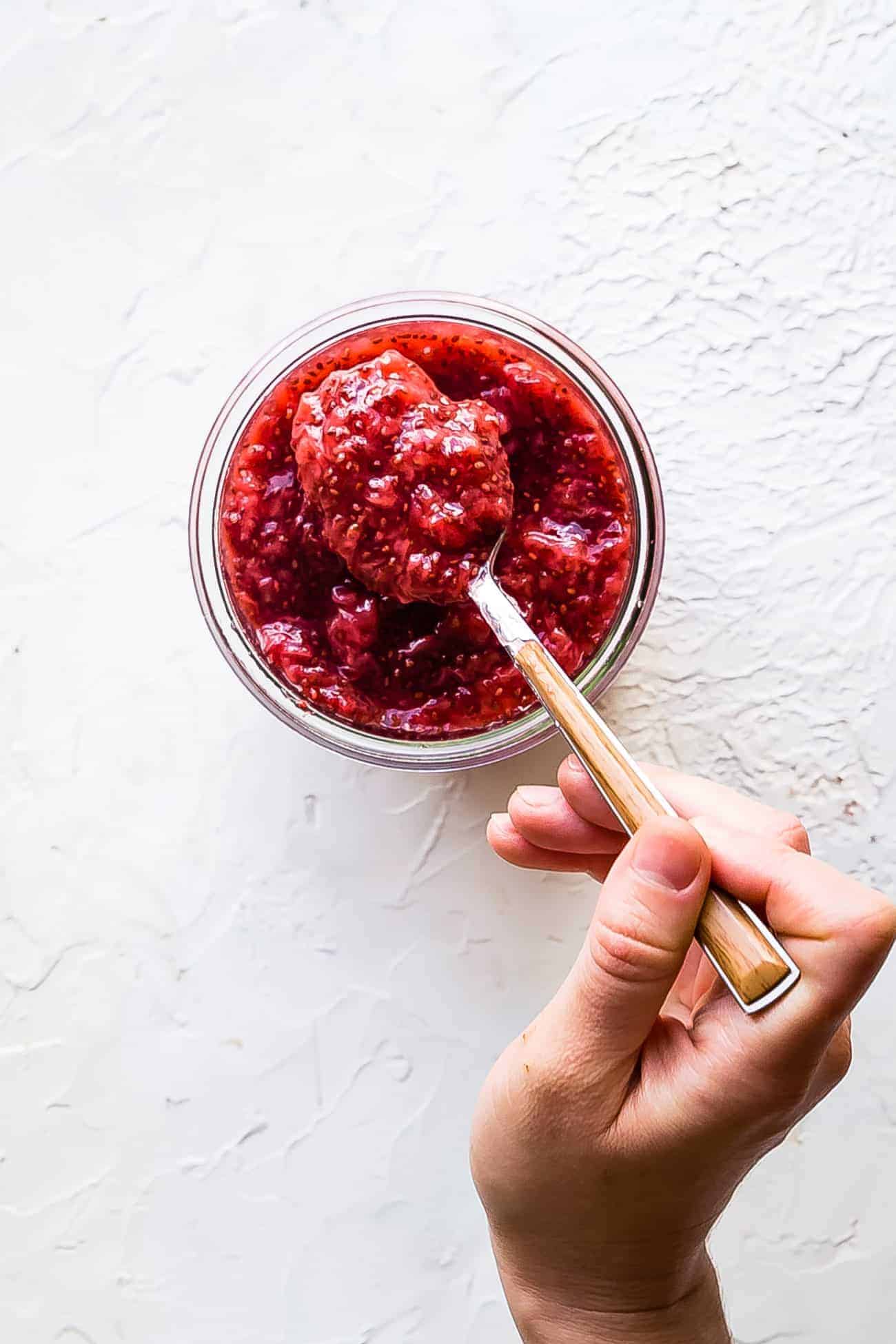 stirring strawberry chia jam in a glass jar