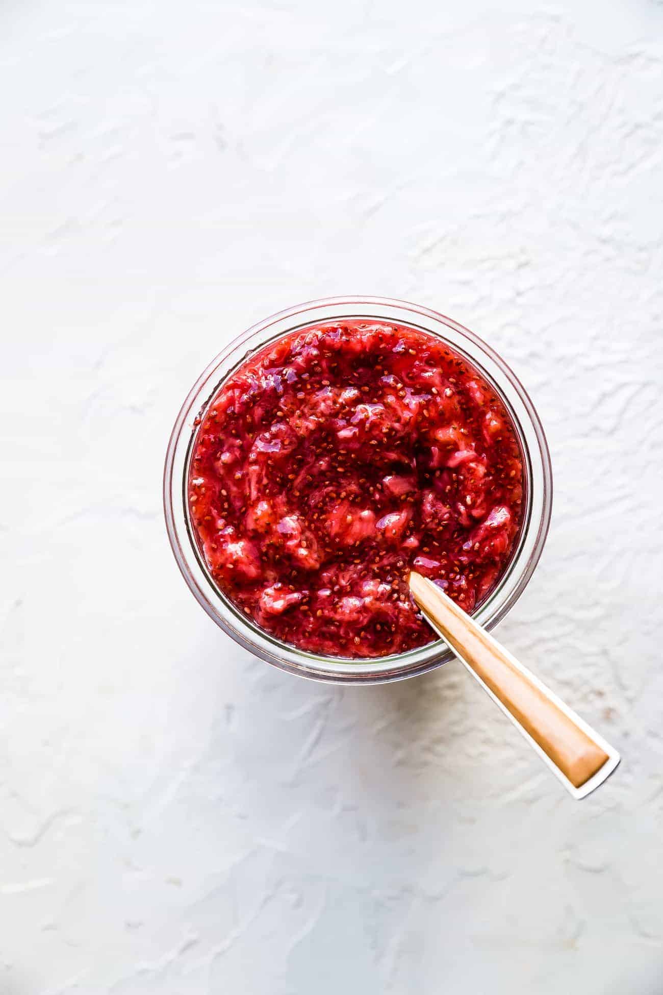 strawberry chia jam in a glass jar with a spoon inside