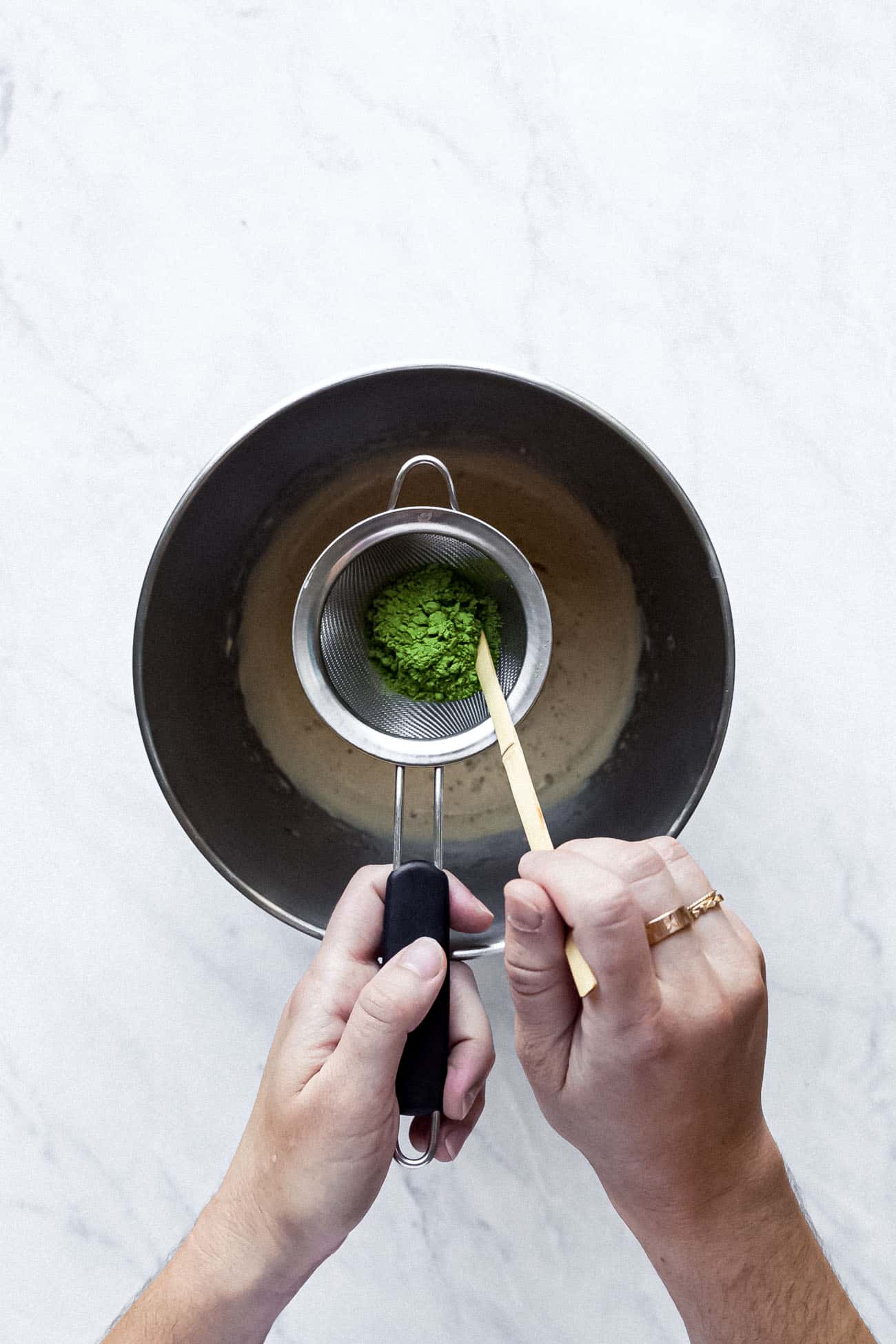 sifting matcha into a large stainless steel bowl