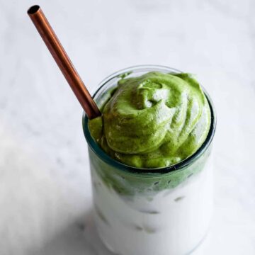 whipped matcha in a glass with milk, ice, and a copper straw