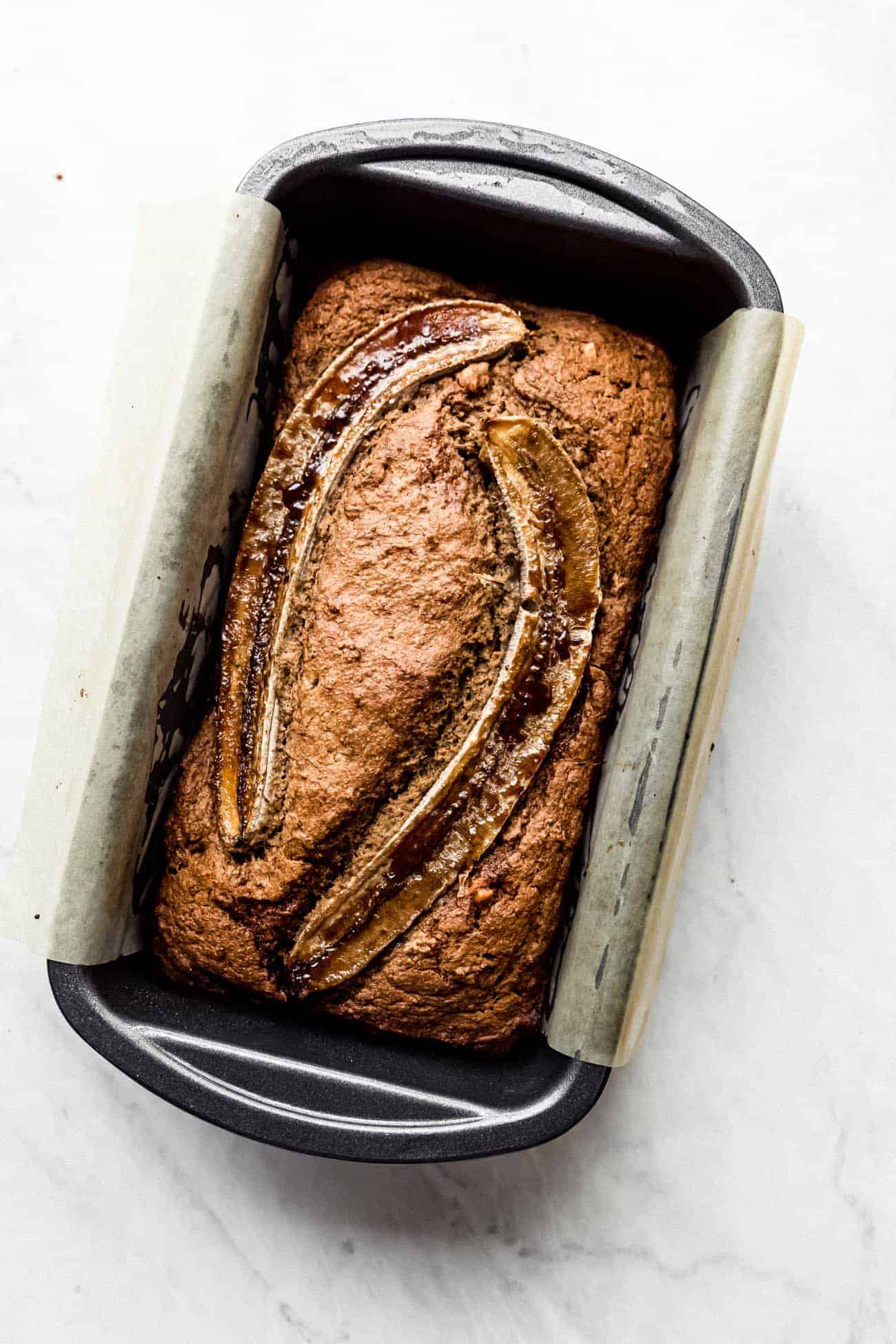 banana bread in a loaf pan with sliced bananas on top